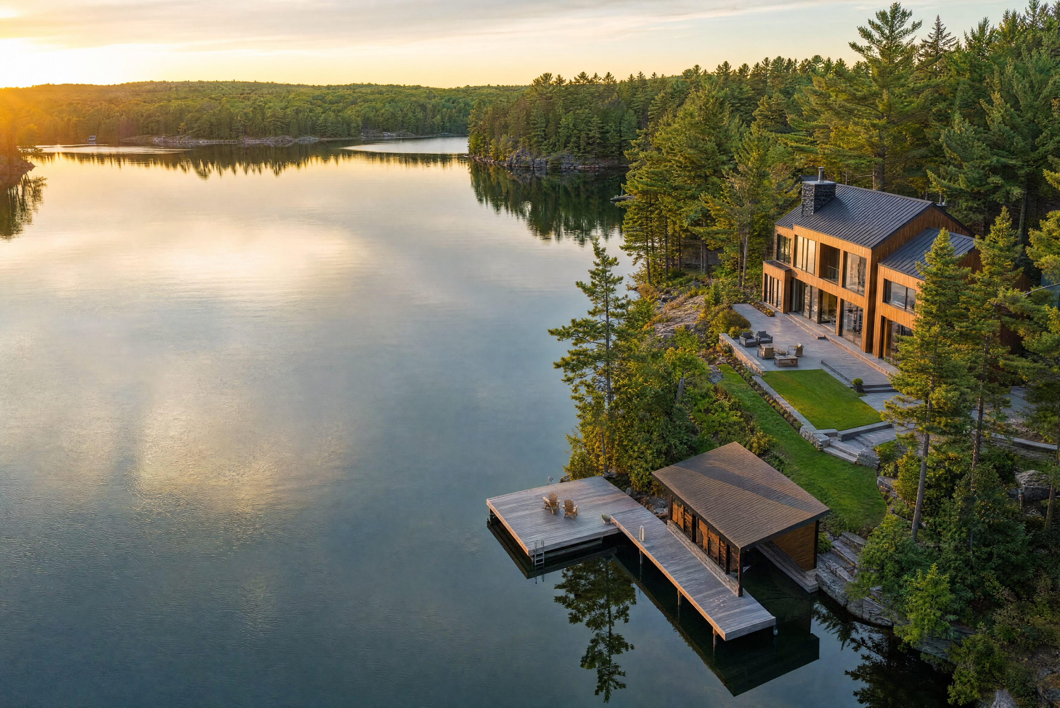A lakeside home at golden hour, photographed from the air with its dock and the tree line